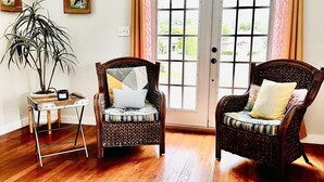 Una habitación con dos sillas de mimbre, una mesita con una planta y una puerta con cortinas.