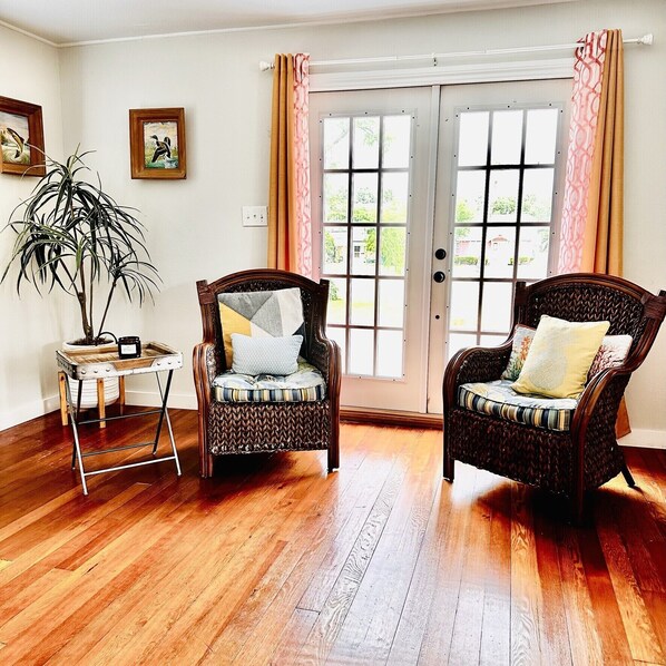 A room with two wicker chairs, a small table with a plant, and a door with curtains.