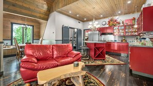 A spacious living area with a red leather sofa, a wooden coffee table, and a dining table. The kitchen features red cabinets and a large island.