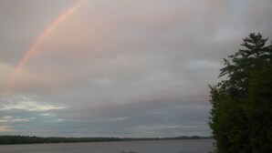 En sø med regnbue, træer og en overskyet himmel.