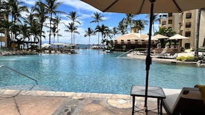 En resort-pool med palmer, liggestole og parasoller.