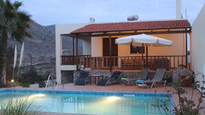 A pool area with lounge chairs and umbrellas, a small table, and a view of a mountain. - Vacation Home in Chania,private Pool beachfront , it is consisted of 2 houses.  (Chania)