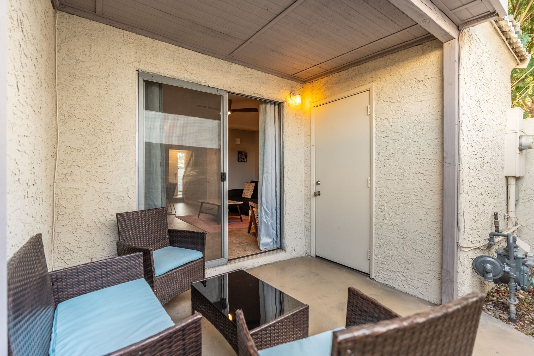 Un patio couvert aménagé avec des meubles en osier et une table en verre.