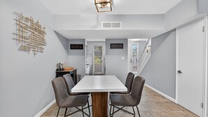 Un espace repas moderne avec une table blanche et quatre chaises, un élément décoratif en bois et un luminaire suspendu au plafond.