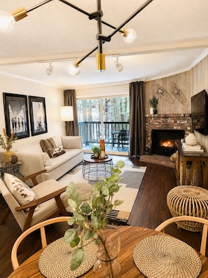 A living room with a sofa, coffee table, and chairs, a fireplace, and a balcony with a view.