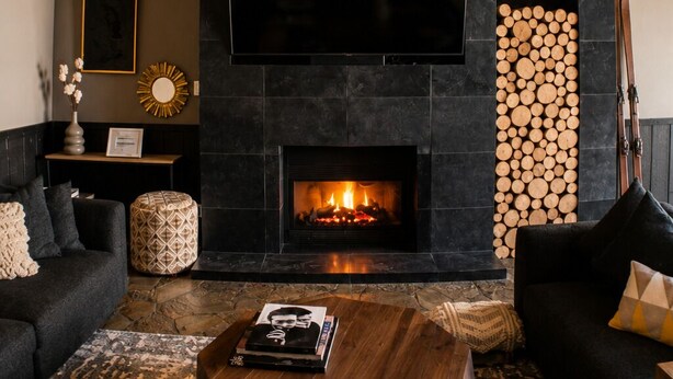 A living room with a fireplace, a flat-screen TV, and a stack of firewood.