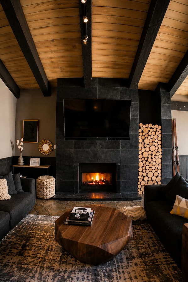Un salon avec une cheminée, un téléviseur à écran plat et une pile de bois de chauffage.