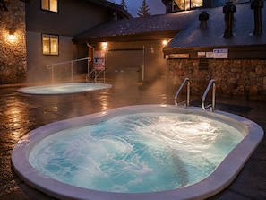 Deux bains Ă remous dont on voit la vapeur sâĂ©chapper, un mur de pierre et lâentrĂ©e dâun bĂątiment avec une enseigne.
