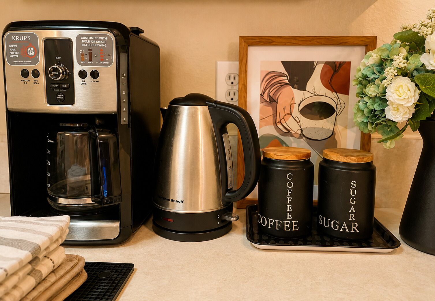 Una cafetera, un hervidor y dos recipientes etiquetados 'Café' y 'Azúcar' sobre una encimera.