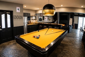 A pool table with a yellow felt surface, a black-framed pool table, and a cue stick in the center.