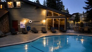 A swimming pool with lounge chairs and a building with large windows and doors.