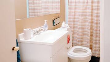 A bathroom with a white sink, mirror, and toilet. There is a striped shower curtain and a small shelf with toiletries.