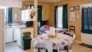 A compact kitchen with a microwave, stove, and sink. A dining table with chairs is in the center, and a ceiling fan is above. - The Ranch Cabin @ Whiskey Mountain Great Location! (Leakey)