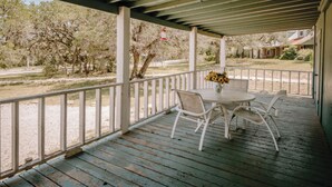 A covered outdoor area with a table and chairs, a railing, and a view of trees and a building in the background. - The Ranch Cabin @ Whiskey Mountain Great Location! (Leakey)