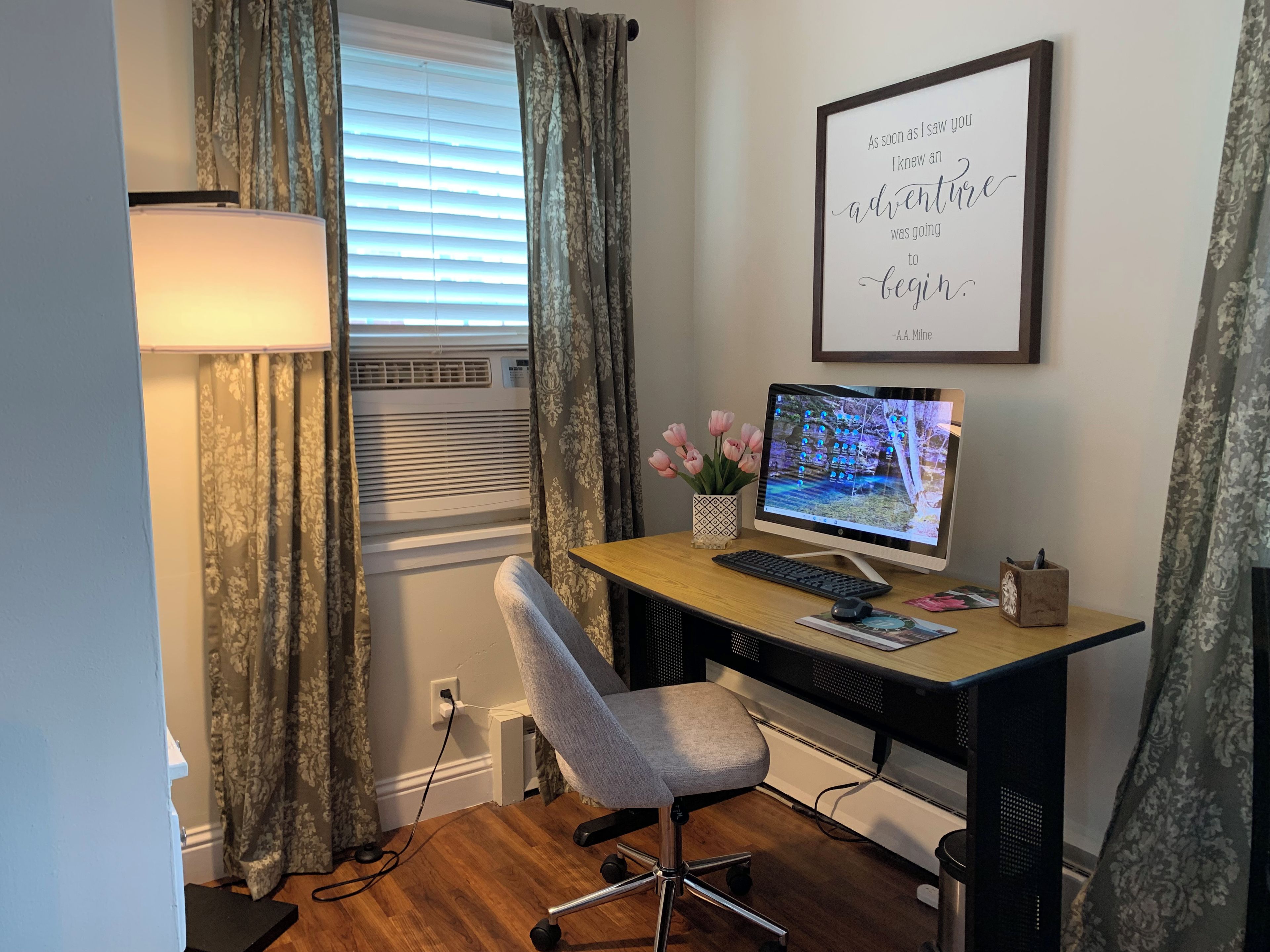 A home office with a desk, computer, chair, and a framed inspirational quote on the wall.