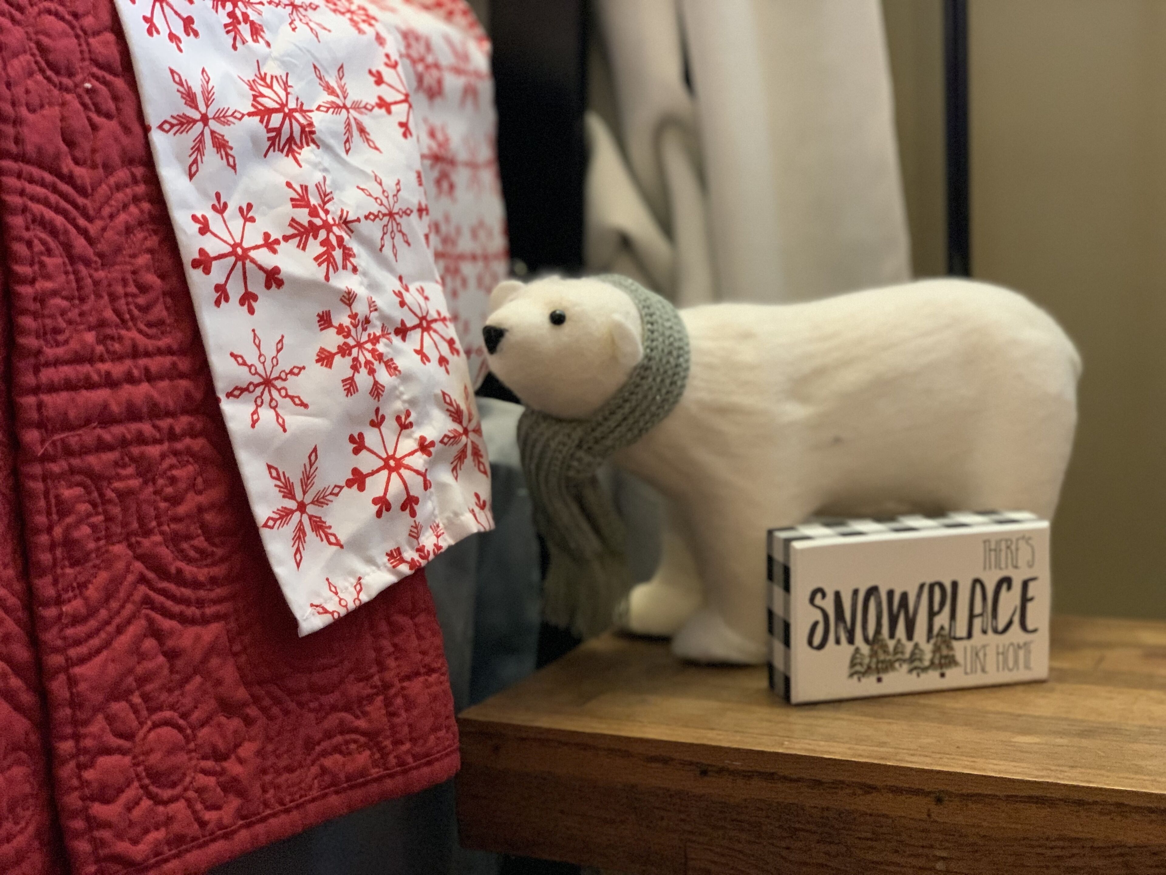 Un peluche de oso polar sobre una superficie de madera, con un cartel que dice 'THERE'S SNOWPLACE LIKE HOME'.