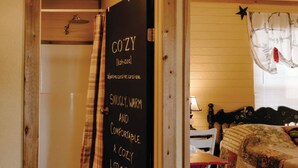 Una habitación acogedora y pequeña con suelo de cuadros, cama con ropa de cama estampada, puerta de madera con un cartel de pizarra y una ventana con un adorno de estrella.