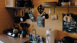 Una cocina con un letrero que dice "Cali Sweet Cabin", una tetera, un lavamanos y varios utensilios de cocina.