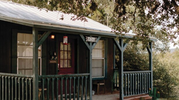 Un edificio rústico de madera con un porche, una puerta roja y un letrero que dice 'COZY'.