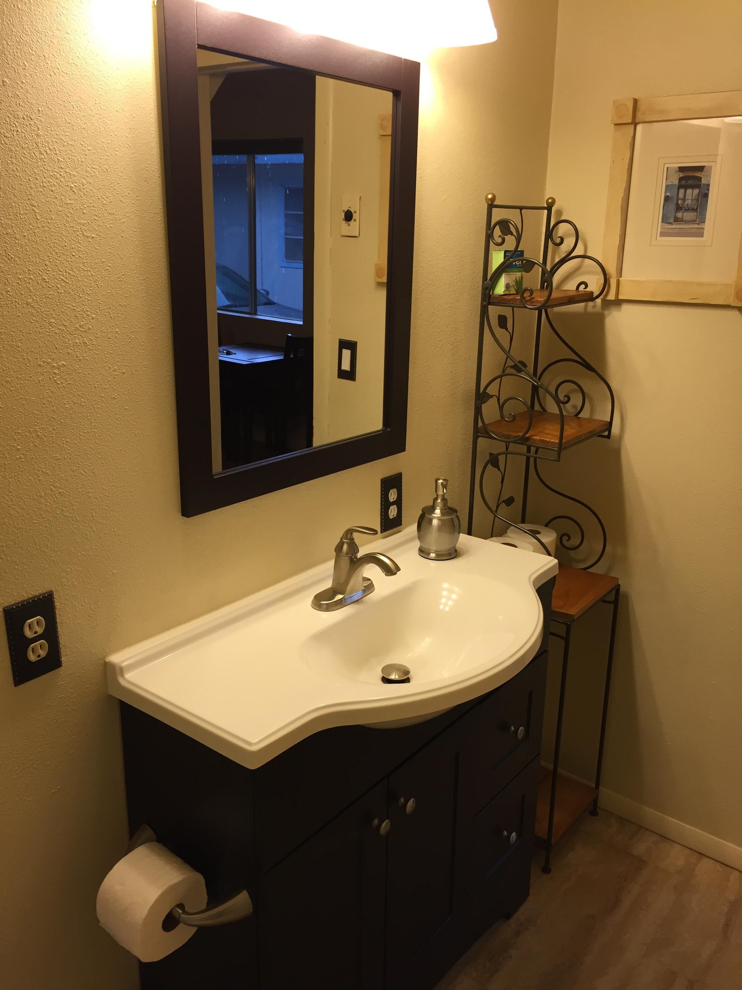 A bathroom with a white sink, a mirror, a toilet paper holder, and a small shelf with toiletries.