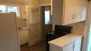 Una cocina compacta con gabinetes blancos, una estufa negra y una puerta que da a otra habitación.