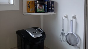 Una cocina con estantes que contienen productos de café y té, un cesto de basura y utensilios de cocina.