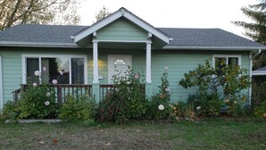 Una casa con fachada verde, un porche delantero y un jardín bien cuidado con diversas plantas y flores.