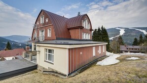 A two-story building with a sloped roof and a balcony, surrounded by snow and mountains. - Penzion Villa Miluška (Spindleruv Mlyn)