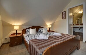Un dormitorio con una cama grande, dos mesitas de noche con lámparas, un cabecero de madera y un espejo en la habitación contigua.