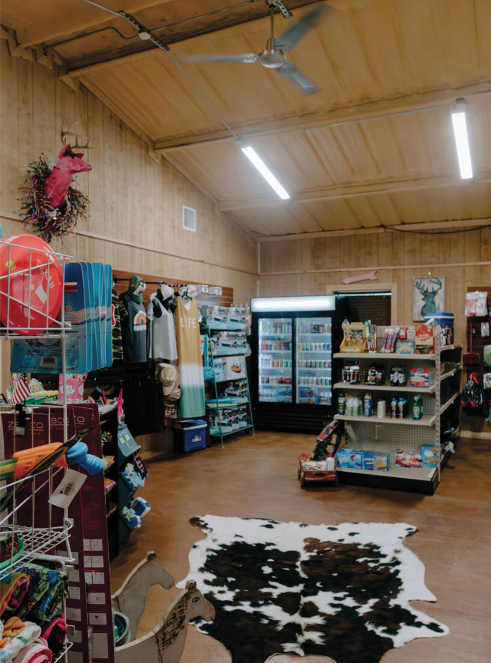 Una tienda con paredes de madera, un ventilador de techo y un refrigerador lleno de productos.