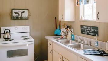 A kitchen with a stove, sink, and cabinets. There is a sign on the wall that says "THIS IS A SELF-CLEANING KITCHEN CLEAN UP AFTER YOURSELF."
