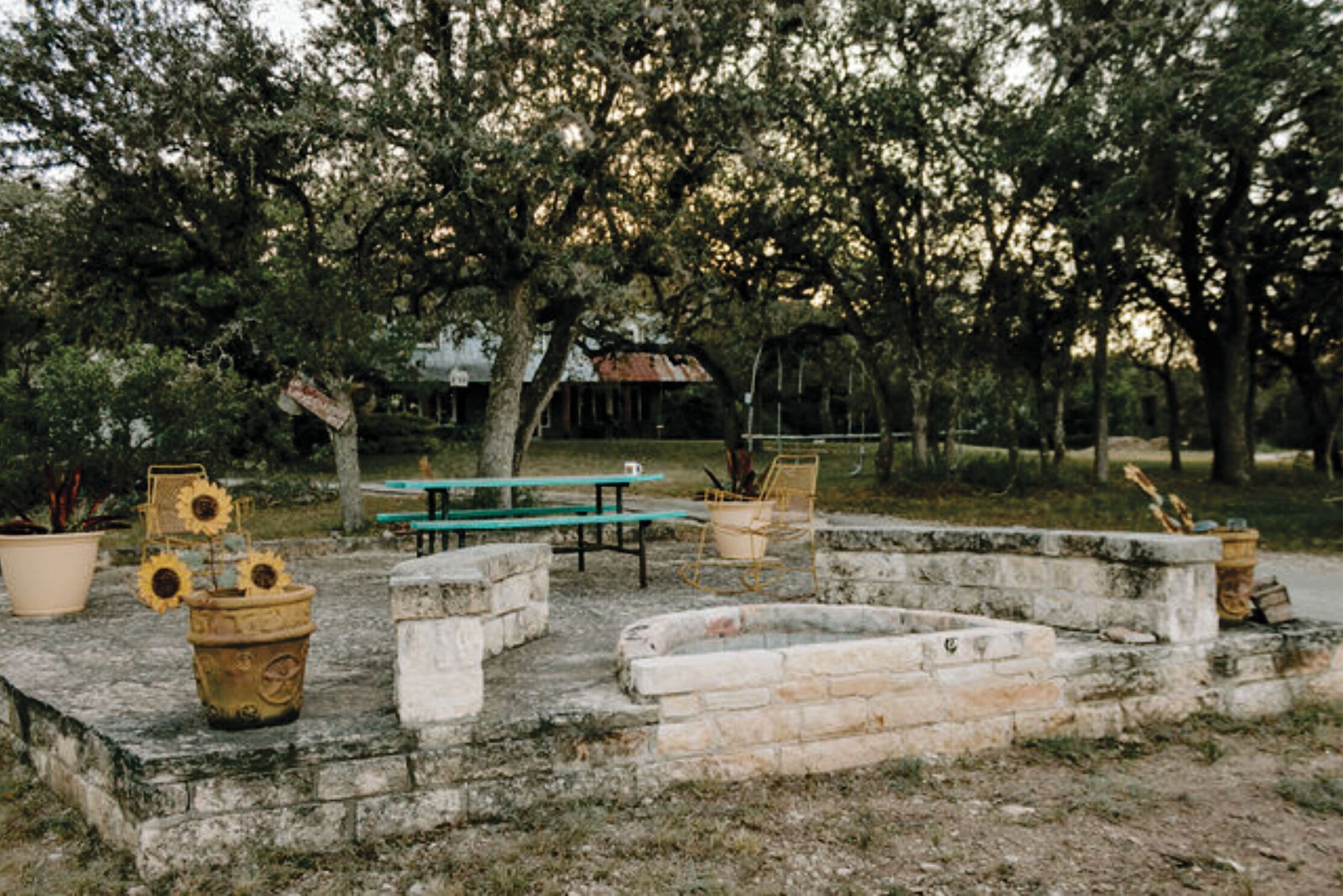 An outdoor seating area with stone benches and tables, surrounded by trees.