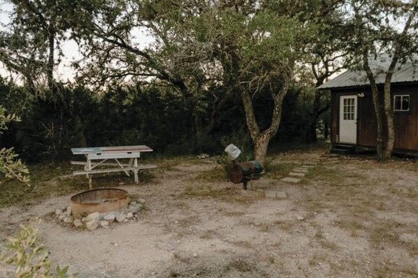A rustic cabin with a wooden exterior, surrounded by trees and a gravel path leading to it.