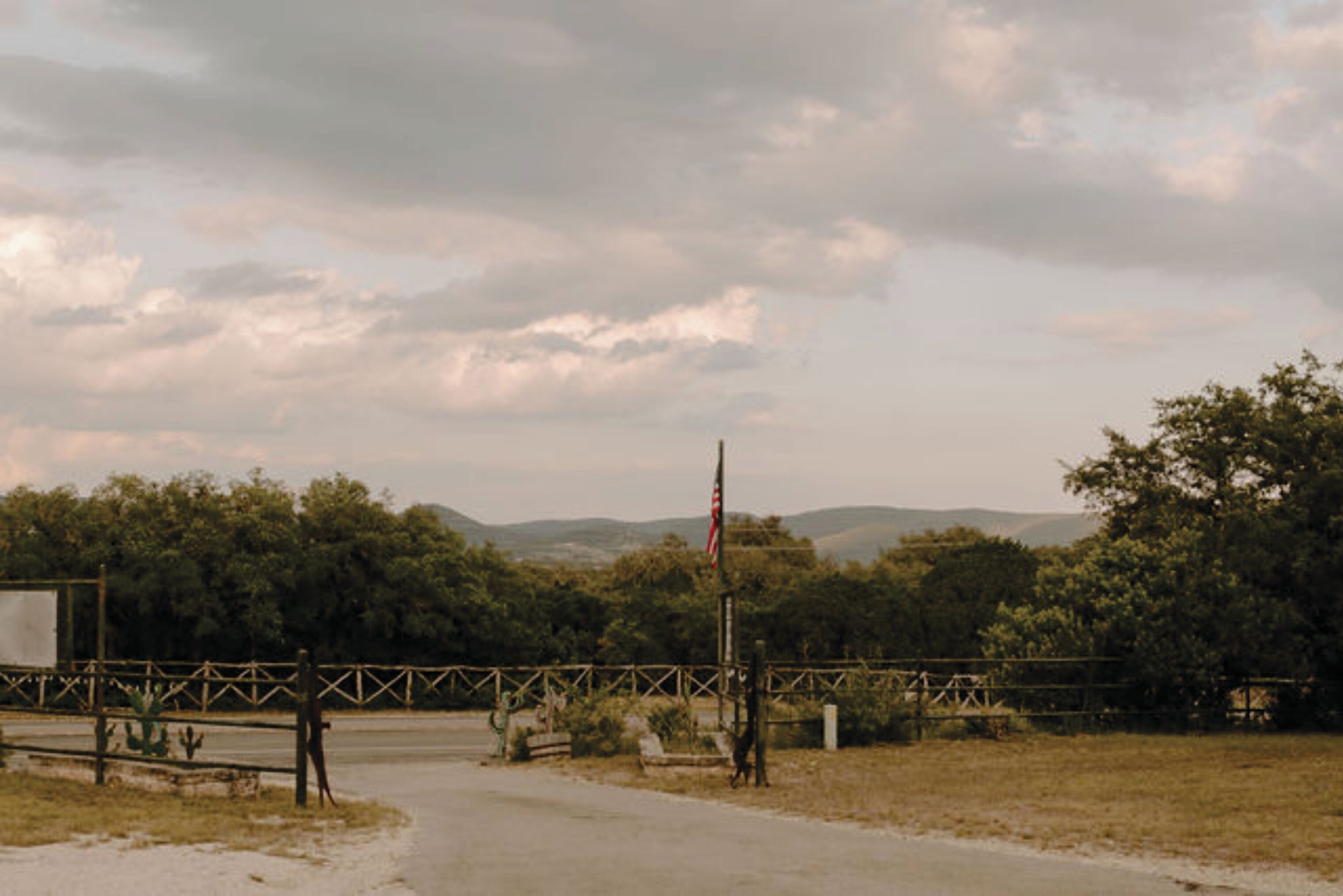A rural road with a wooden fence and a flagpole.