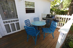 Eine überdachte Veranda mit Grill, blauen Stühlen und einem kleinen Tisch.