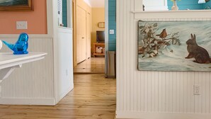 Un couloir avec un plancher en bois, un mur bleu et un tableau représentant un lapin et un oiseau.