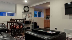 A modern living room with a leather sofa, a coffee table, and a dining area with a chair and a shelf. - Dartt's Park Garden View - 1 Bedroom (Owatonna)