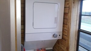 Une petite buanderie équipée d’un lave-linge et d’un sèche-linge à chargement frontal, avec des murs en bois et une fenêtre.
