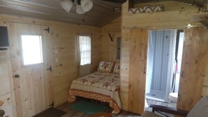 Une pièce de cabane en bois comprenant un lit, une petite table, une chaise et un ventilateur de plafond.