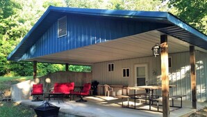 A covered outdoor patio with red chairs, a table, and a fire pit.