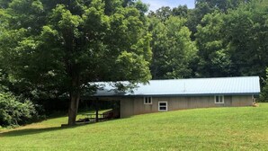 A single-story building with a blue roof, surrounded by a grassy field and trees.