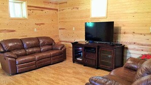 A wooden-paneled room with a brown leather sofa, a television on a stand, and a small cabinet.