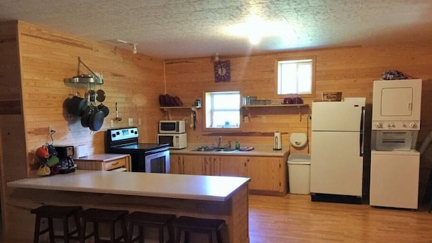 A kitchen with wooden cabinets, a central island with stools, a microwave, a refrigerator, and a stove.