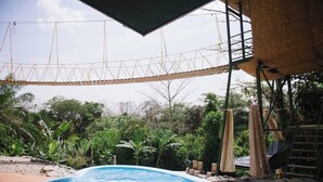 A swimming pool with a rope bridge overhead, surrounded by lush greenery and a thatched-roof structure. - Jungle Family Villa in Quepos: Pool, Waterslide & Zipline — Sleeps 6-8 (Parrita)