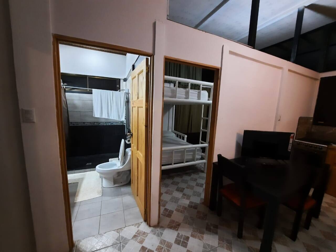A compact room with a bed, a small table, and a television. There is a bathroom visible through an open door.