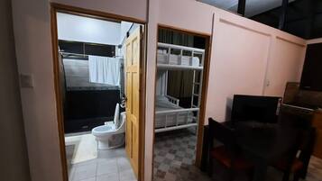 A compact room with a bed, a small table, and a television. There is a bathroom visible through an open door.