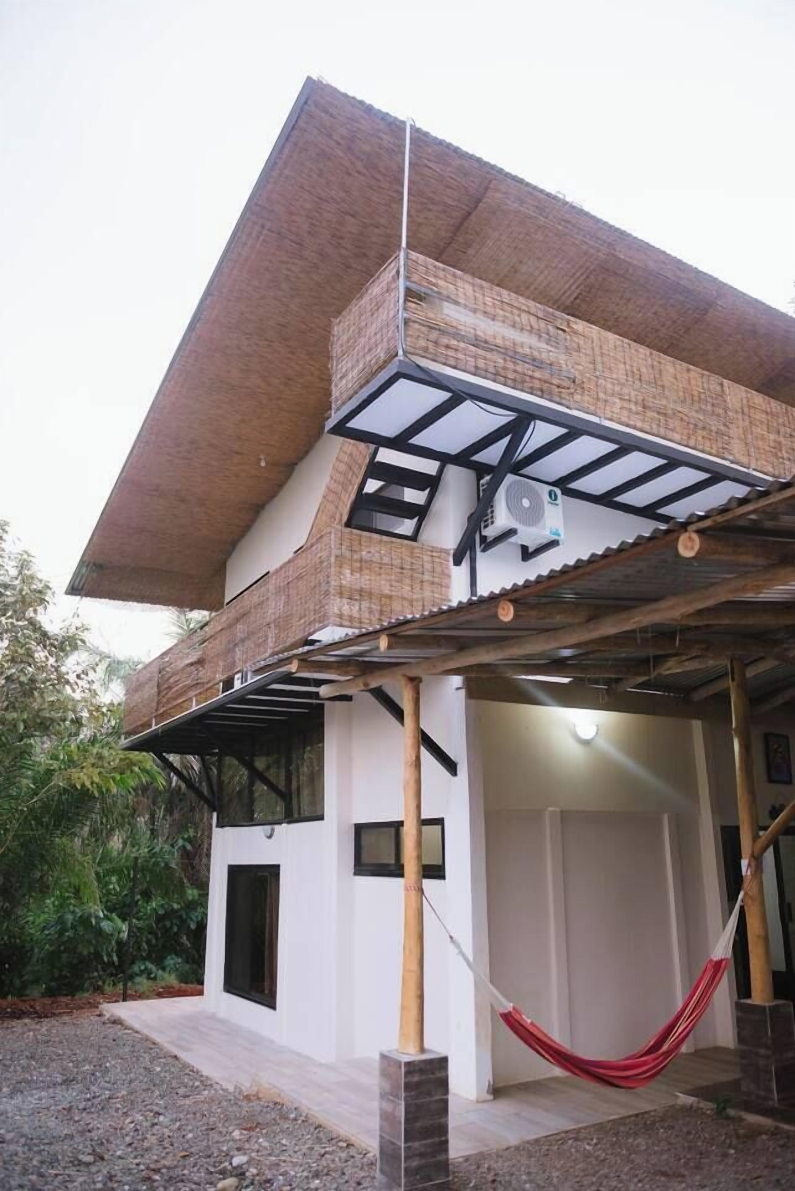 A modern house with a large balcony, a hammock, and a fan.