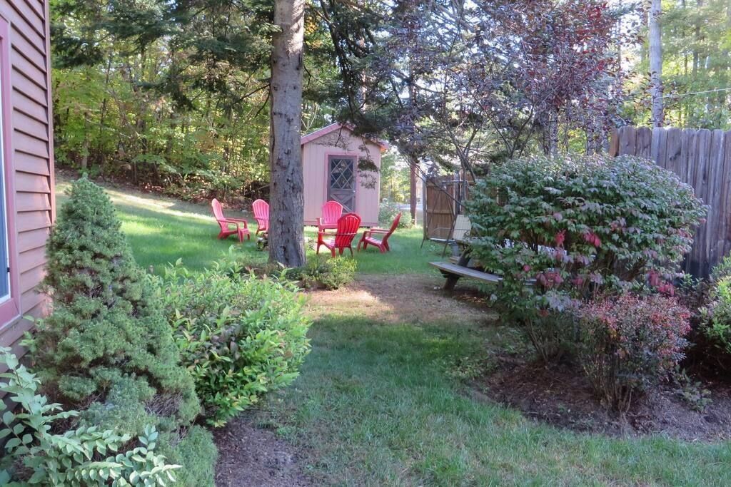 A backyard with a wooden shed, red chairs, and a picnic table.