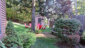 Patio con un cobertizo de madera, sillas rojas y una mesa de picnic.