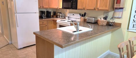 Una cocina con armarios de madera, un refrigerador blanco, un microondas, una estufa y un lavabo.